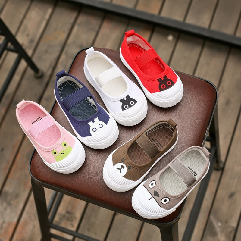 Six canvas kids' Mary Jane shoes in pink, navy, white, red, brown, and grey with animal faces on the toes.