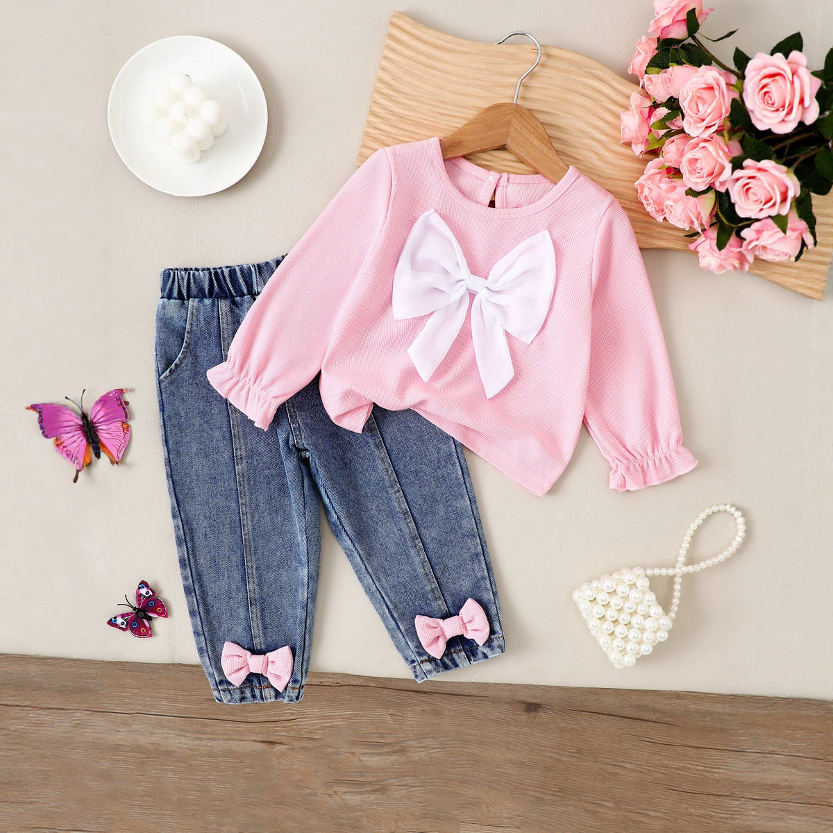 Pink ribbed long-sleeve top with large white chest bow and blue denim jeans with pink ankle bows.