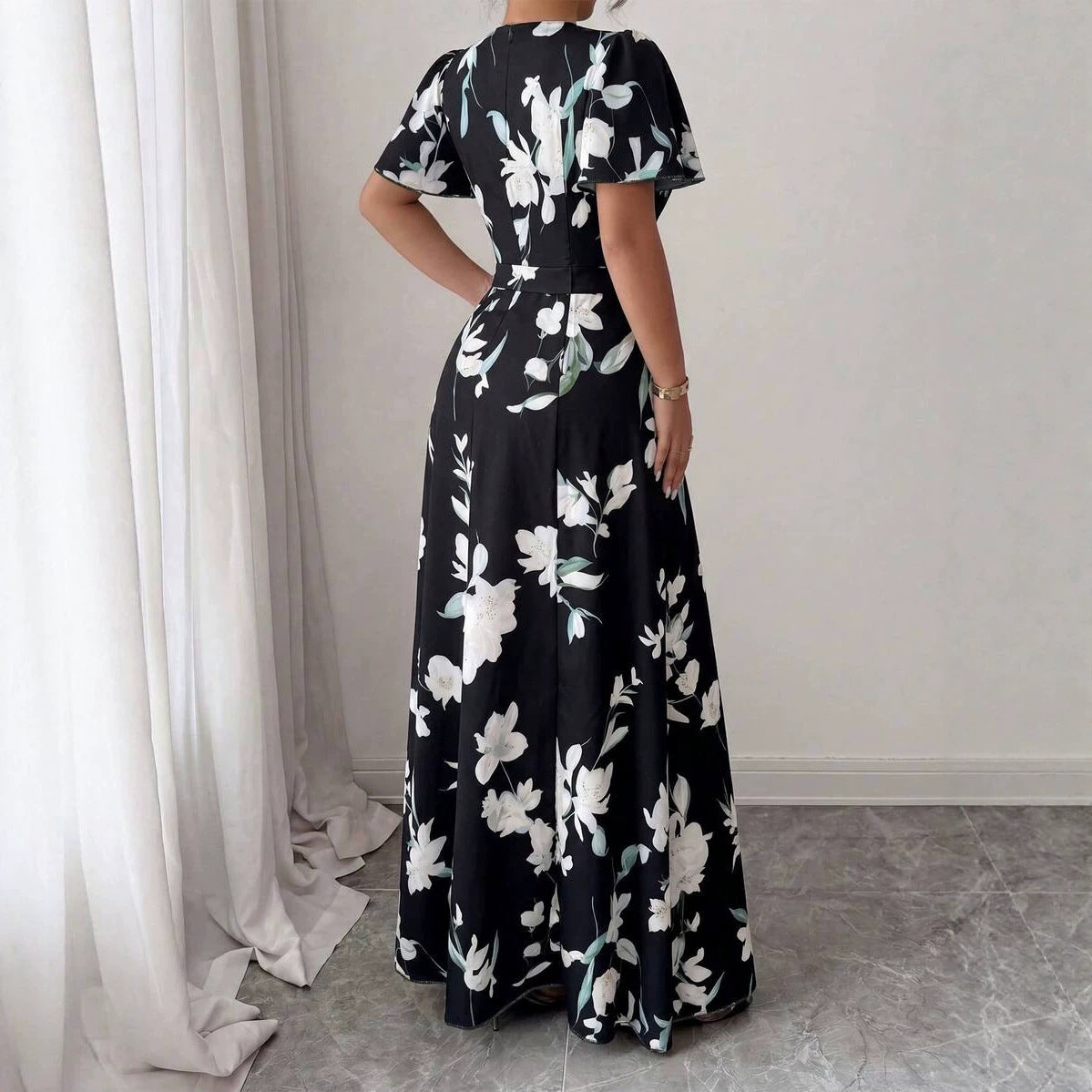 Back view of a black maxi dress featuring a white floral pattern, short sleeves, and a belted waist.