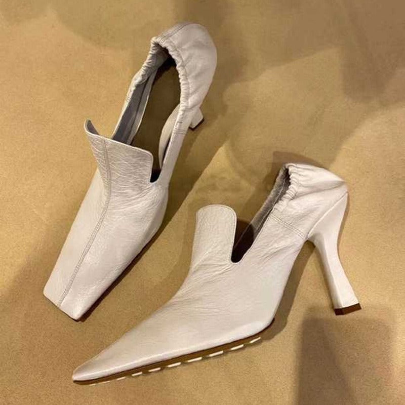 White leather stiletto mules with a square toe, gathered heel collar, and distinct architectural mid-height heel.