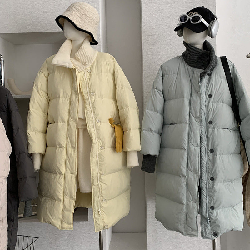 Two mannequins wear long puffer coats with stand-up collars, one in pale yellow and the other in light blue.
