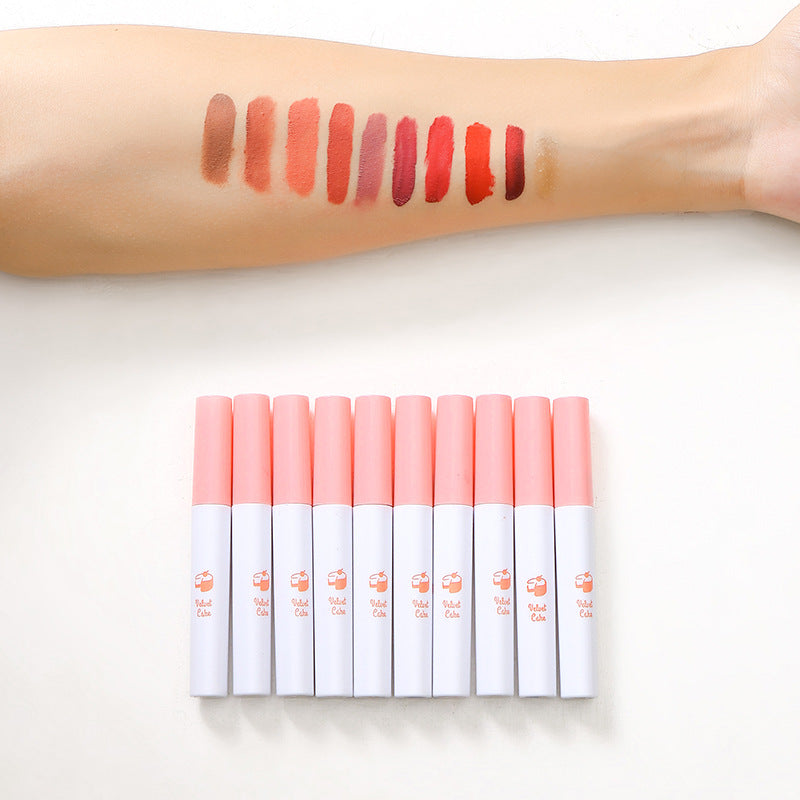 Ten vertical white and pink plastic lipstick tubes with peach graphics, shown with ten swatches on an arm.