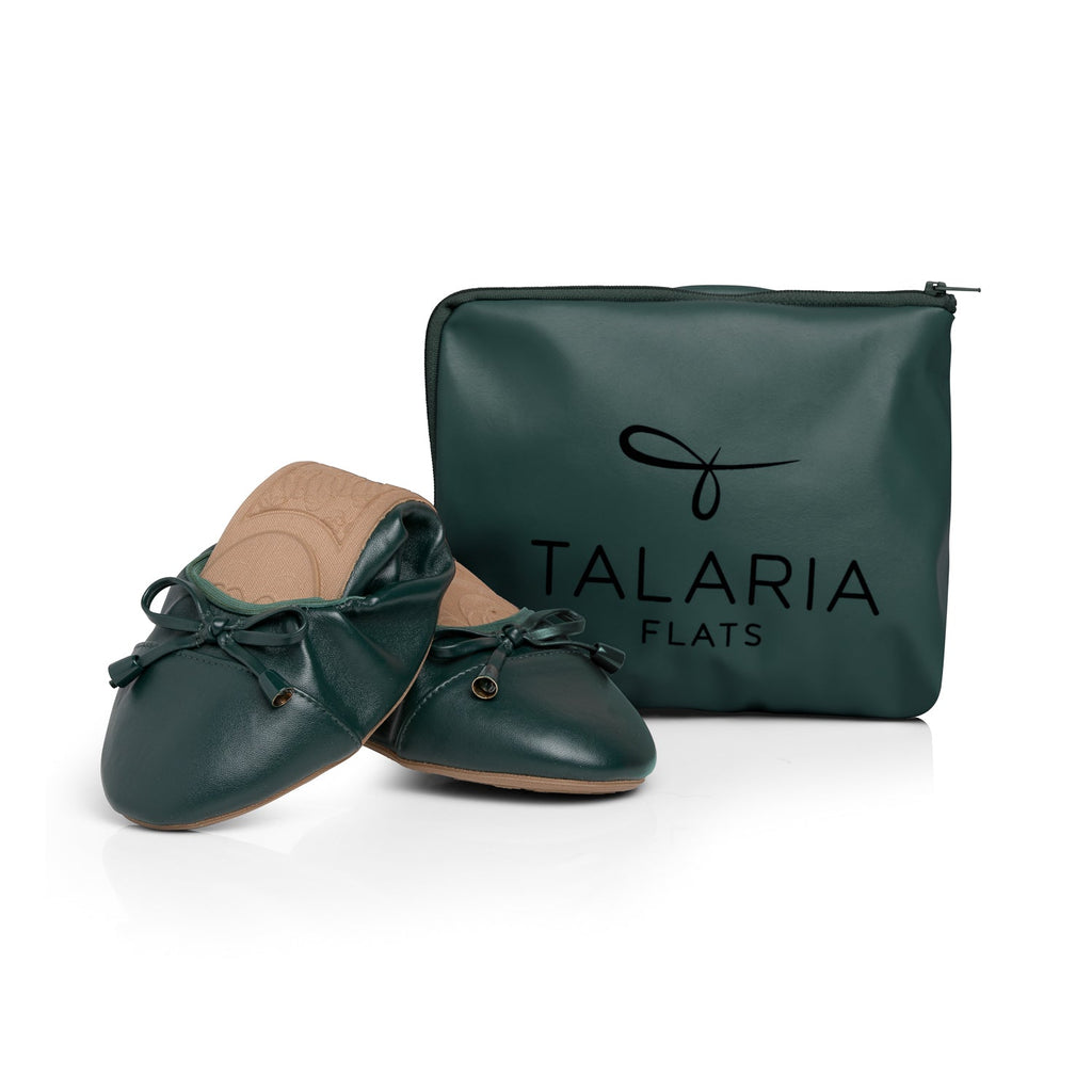 Green Talaria Flats footwear with premium evergreen color, folded in front of a bag, showcasing stylish and comfortable shoes.