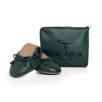 Green Talaria Flats footwear with premium evergreen color, folded in front of a bag, showcasing stylish and comfortable shoes.