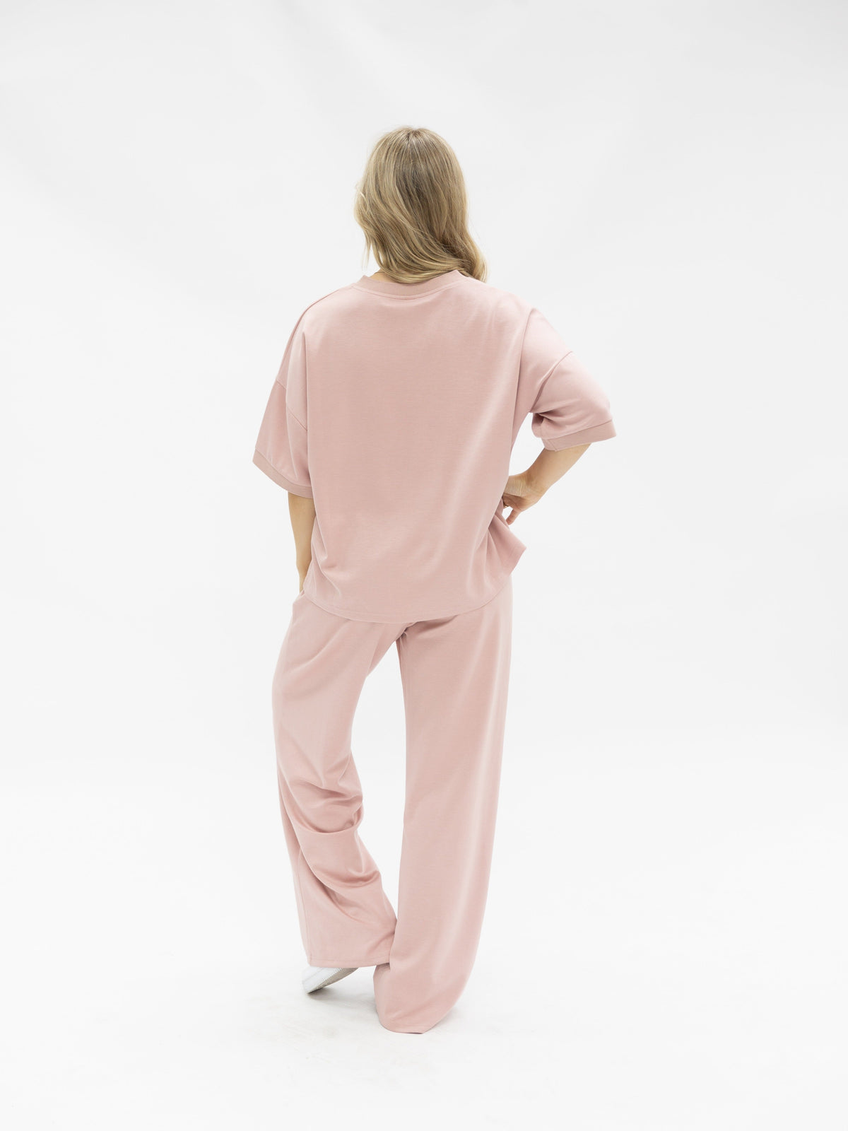 A woman seen from behind, wearing pink wide-leg pants and a matching short-sleeve top against a white background.