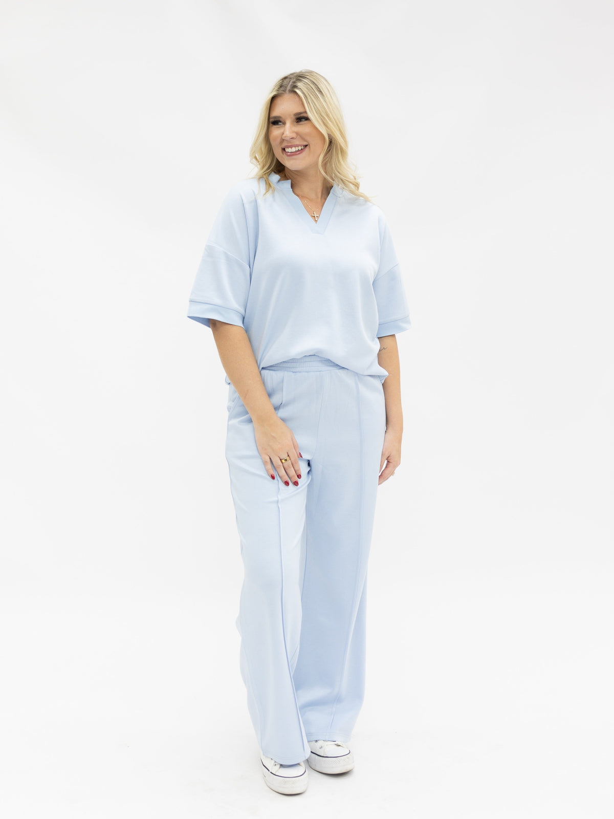 A woman wears matching light blue wide-leg pants and a short-sleeve V-neck top against a white background.