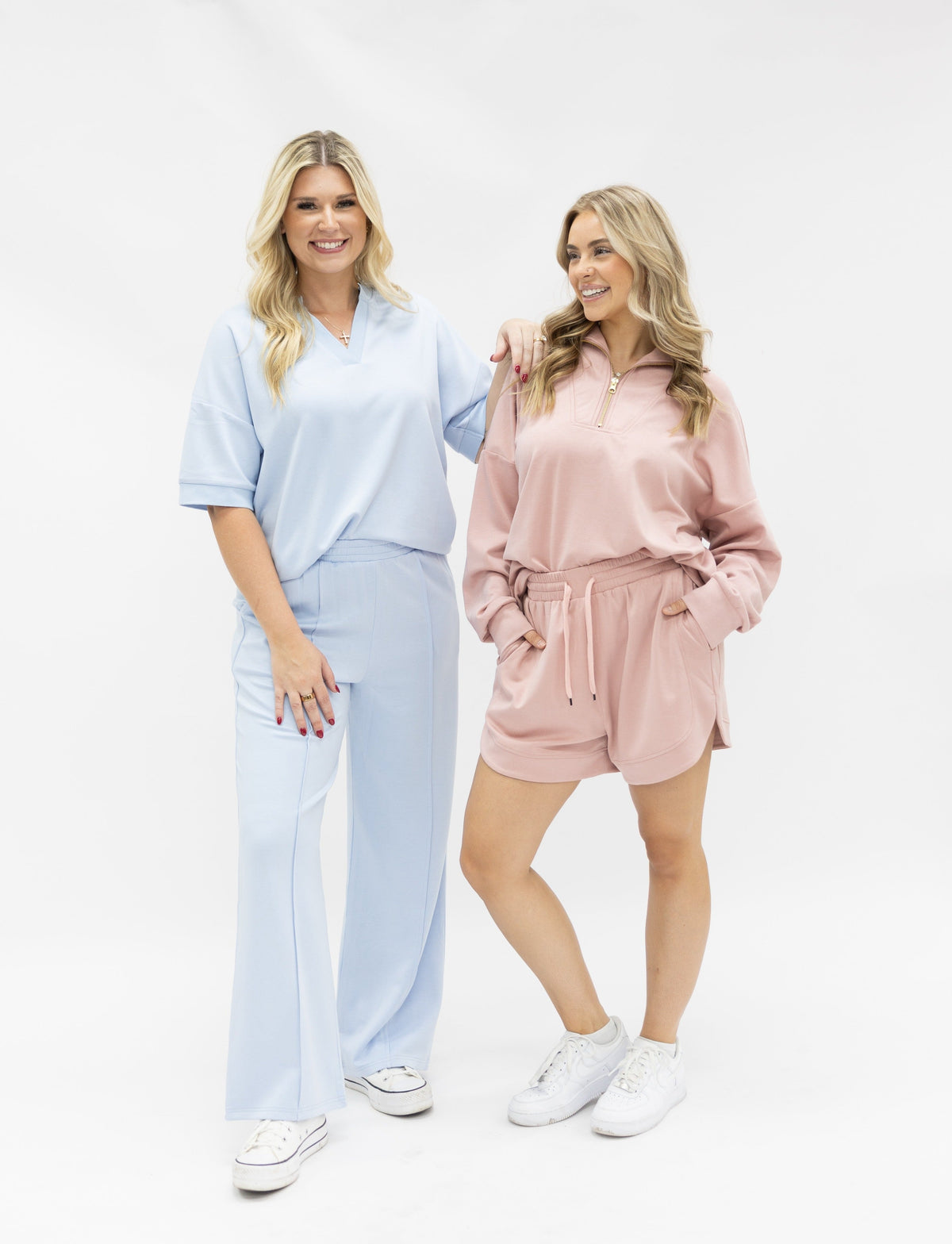 Two smiling women pose in blue and pink lounge sets against a white background.