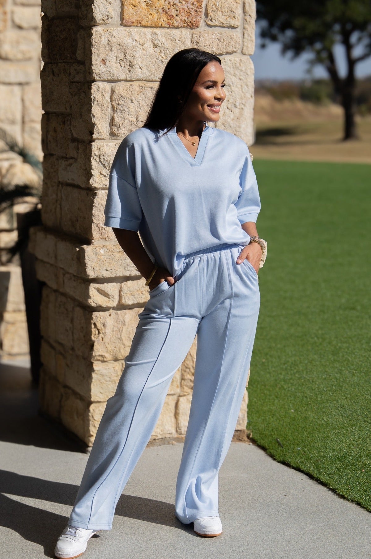 A woman wears loose, light blue pants with front center seams and pockets, paired with a matching top.