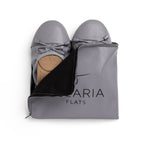 Talaria Flats premium stone grey shoes inside a bag, showcasing their sleek design and comfortable slip-on style.
