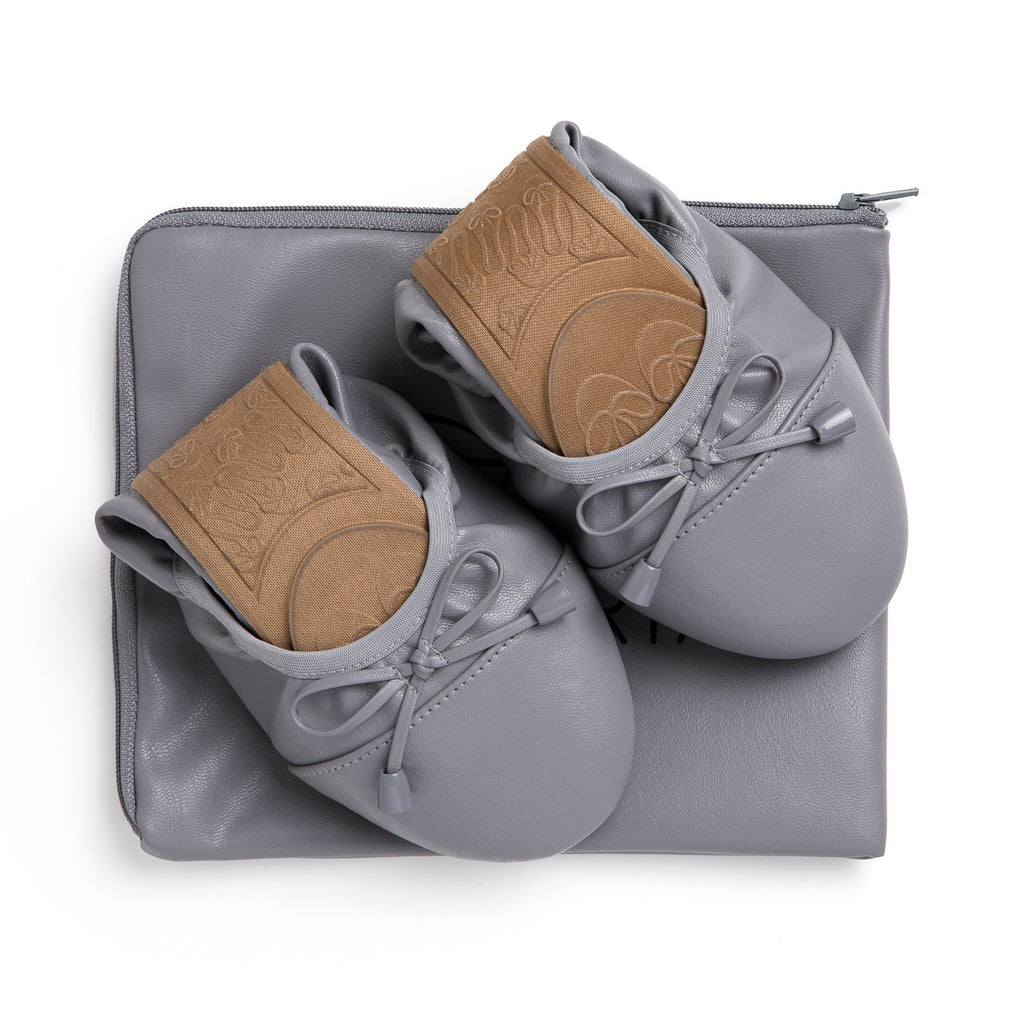 Talaria Flats in stone grey, stylish shoes placed on top of a bag, showcasing their sleek design and comfortable fit.