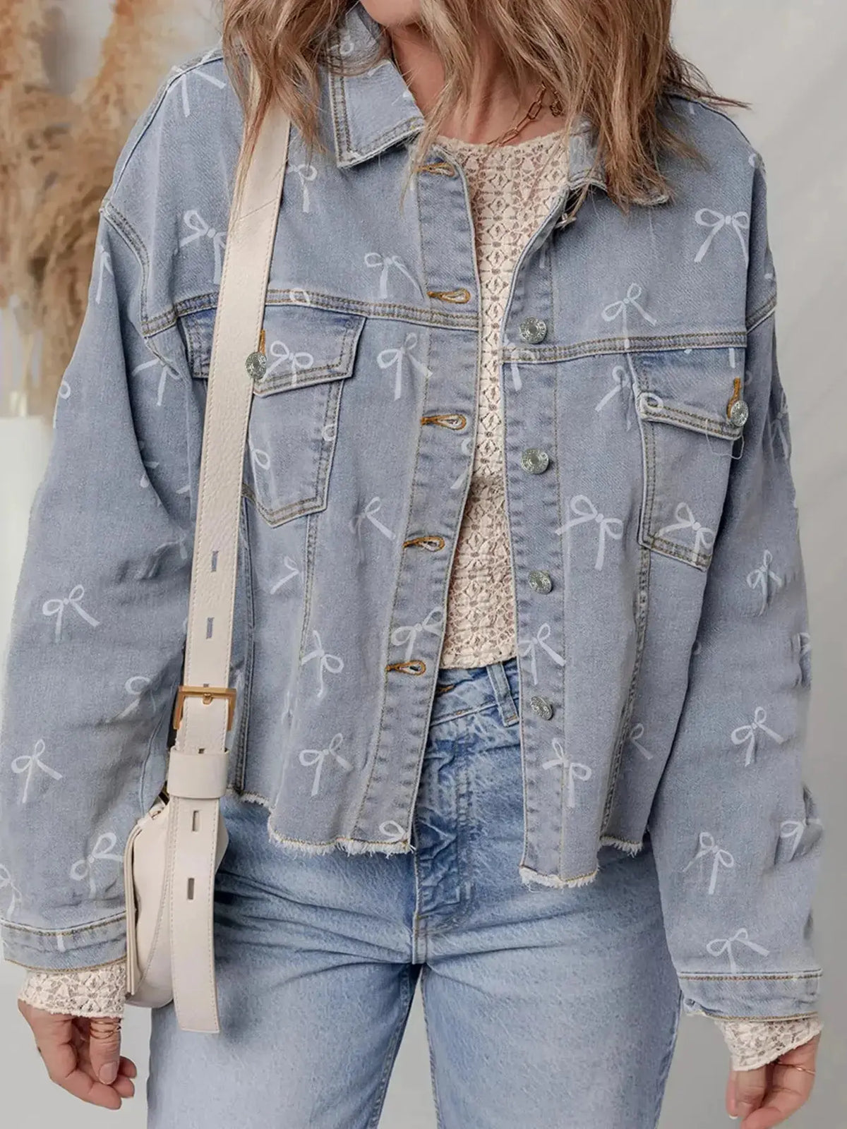 Women’s light wash denim jacket with bow knot print, raw hem, and casual style by Plush Fashion Hub.