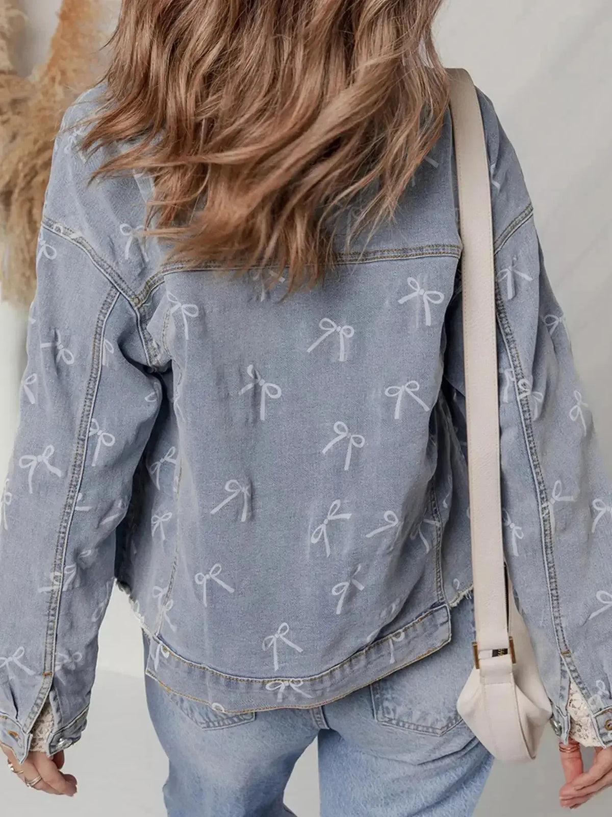 Women’s light wash denim jacket with bow knot print and raw hem, from Plush Fashion Hub, styled with casual fashion.