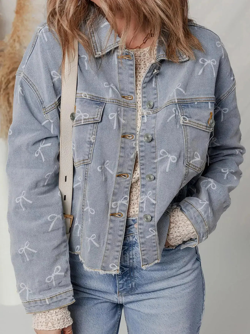 Women’s light wash denim jacket with bow knot print, raw hem, and classic denim style by Trendsi.