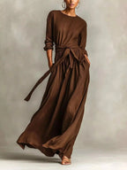 Plus size women's long sleeve maxi dress with tie waist and pockets, by Trendsi, shown on a model with a flowing fabric design.