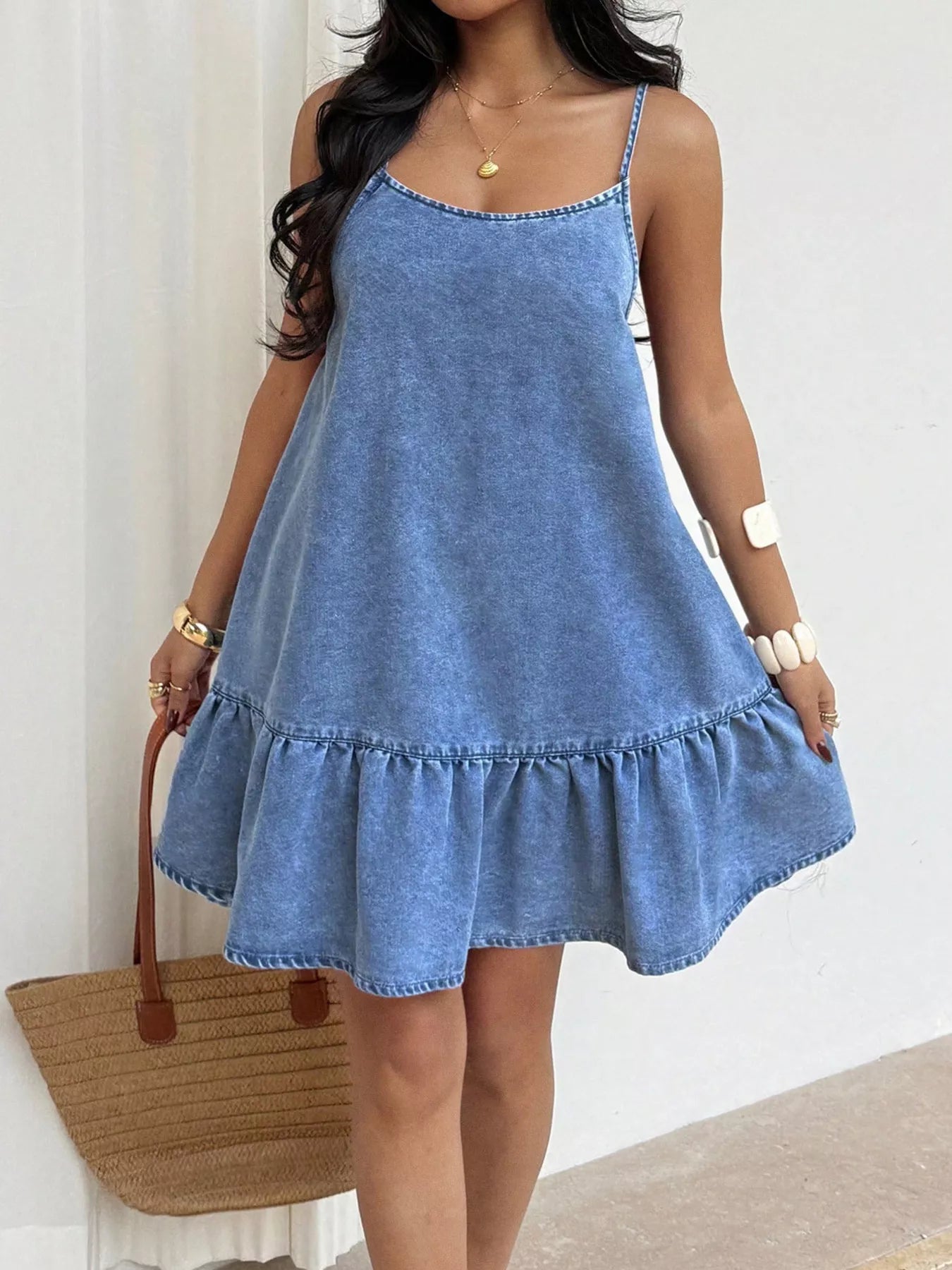 Casual denim spaghetti strap dress with ruffle hem by Plush Fashion Hub, shown on a model in a stylish outdoor setting.