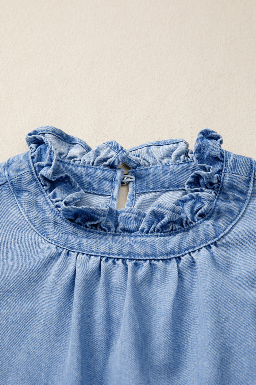 Women's distressed denim top with frilled collar and flutter sleeves, featuring a trendy, casual design.