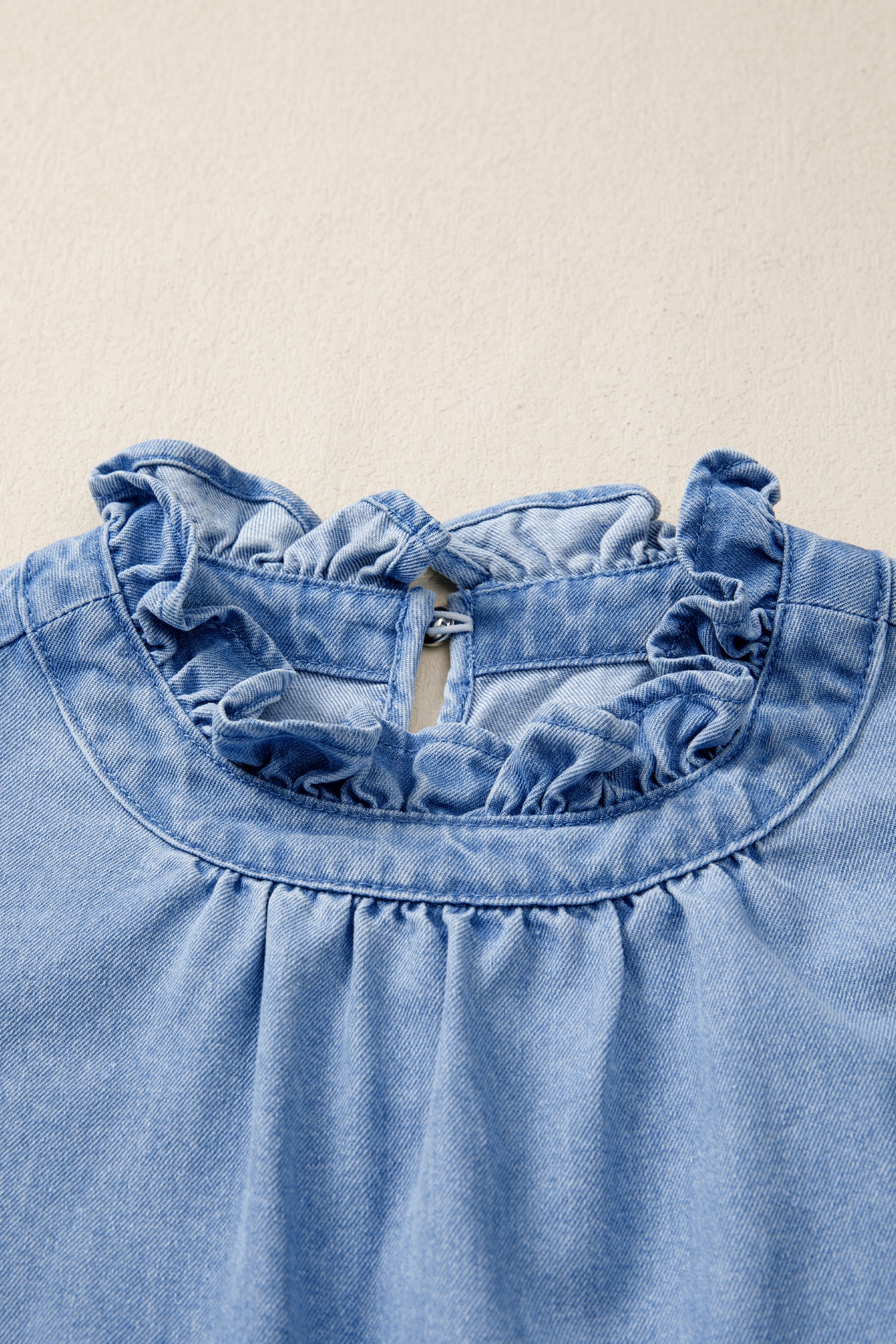 Women's distressed denim top with frilled collar and flutter sleeves, featuring a trendy, casual design.