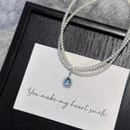 Double layered pearl necklace with teardrop pendant from Shopimist, featuring elegant white pearls and a delicate teardrop charm.