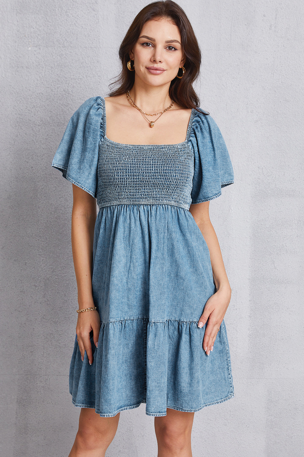 VYSN smocked square neck mini denim dress displayed on a hanger, showcasing a stylish sleeveless design with a fitted waist.