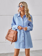 VYSN raw hem button-up denim dress hanging on a wooden hanger, showcasing its casual style and distressed hem detail.
