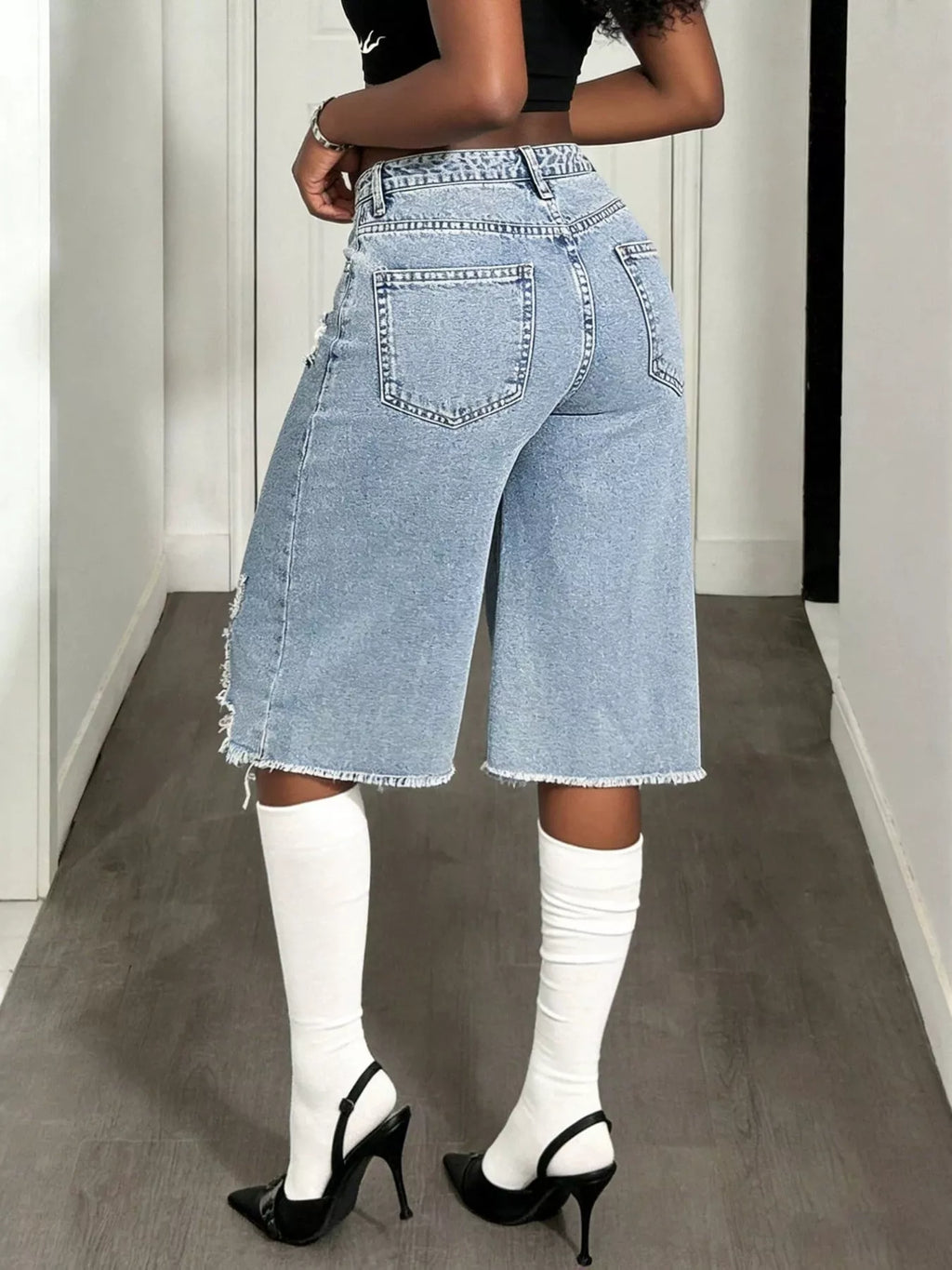 Distressed wide-leg denim shorts by Shopimist with frayed edges and a relaxed fit, shown hanging on a wooden background.