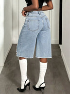 Distressed wide-leg denim shorts by Shopimist with frayed edges and a relaxed fit, shown hanging on a wooden background.