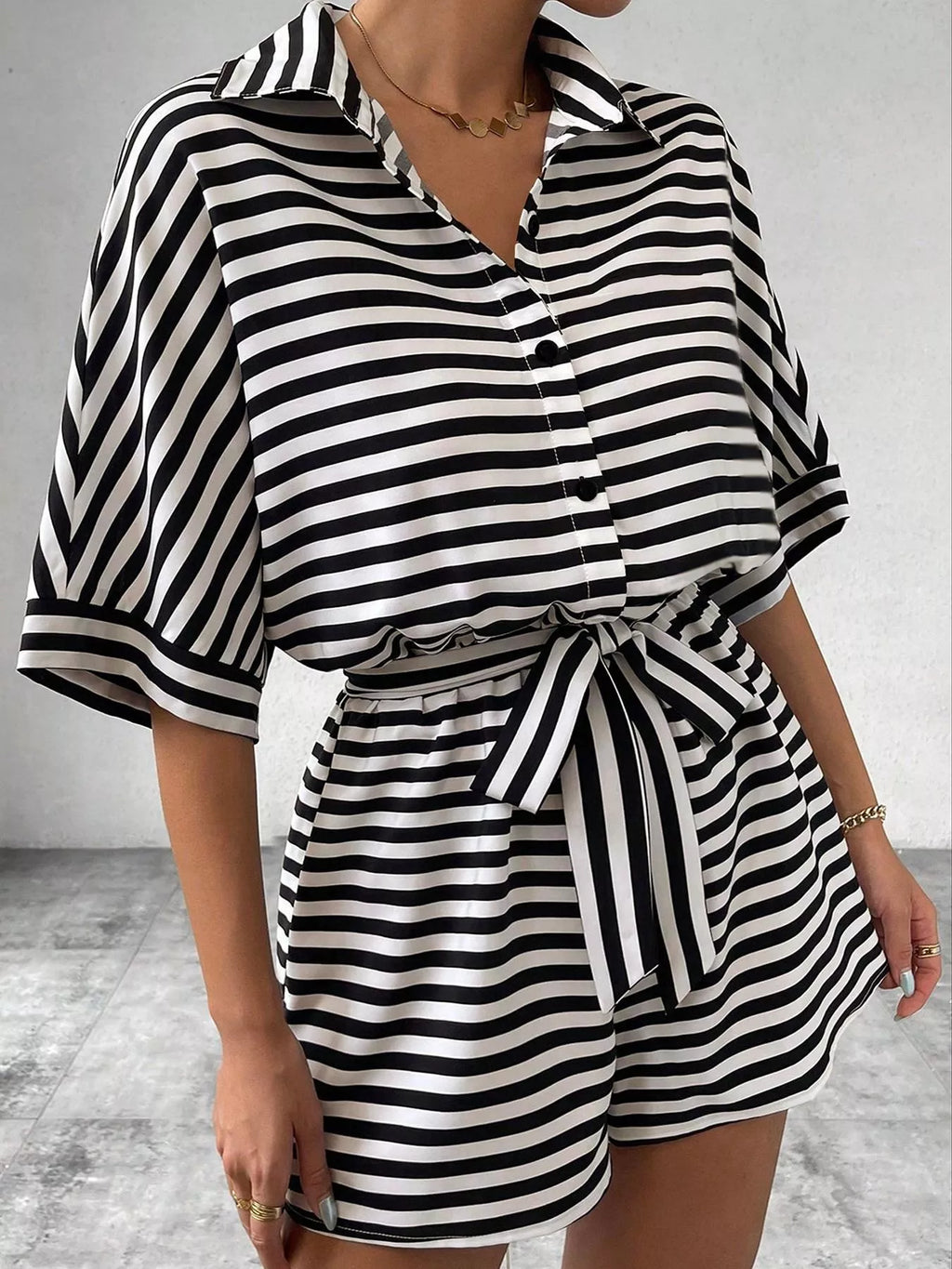 Striped button-up belted romper jumpsuit from Trendsi, featuring a stylish design with a waist belt and short sleeves.