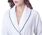 Knee-length white waffle robe for women with piping, made by Plush Fashion Hub, displayed hanging on a hook.